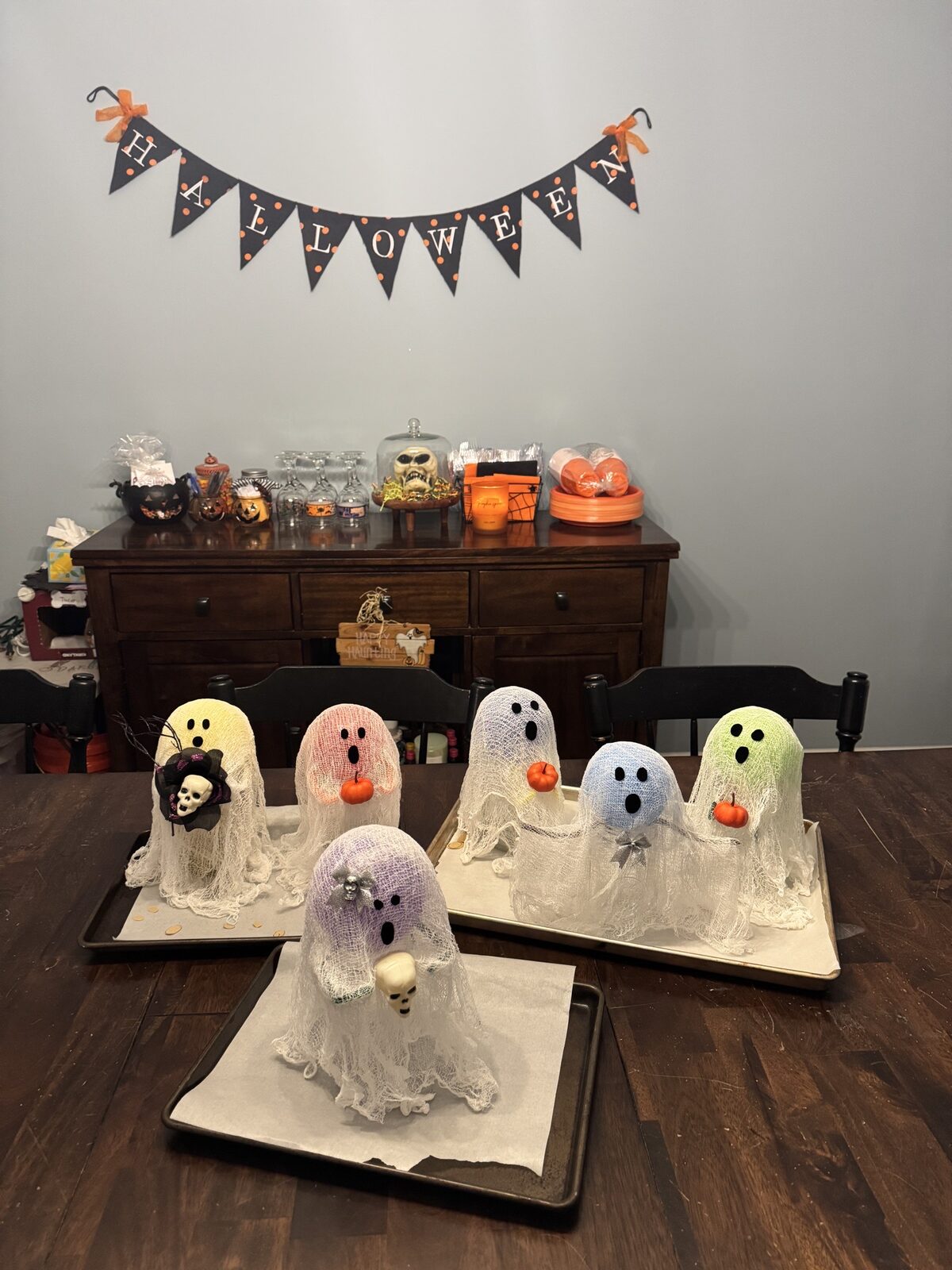 Finished cheesecloth ghosts lined up on a dining table under a Halloween banner