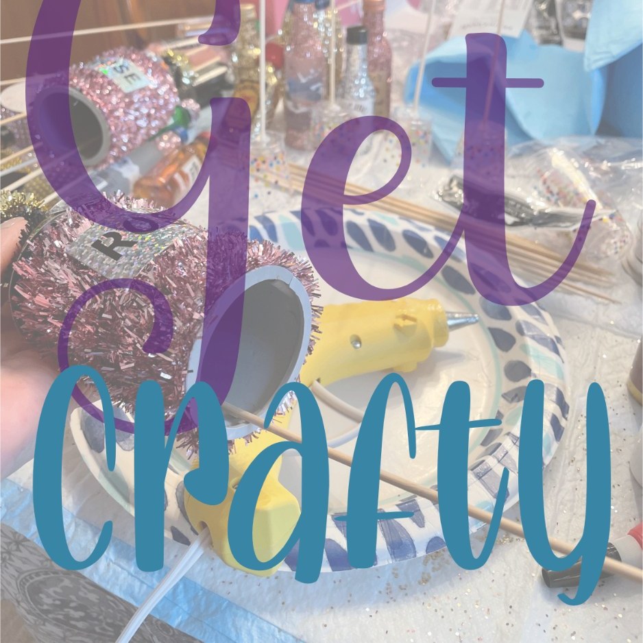 Craft table mid-project with a hot glue gun, glitter bottles and pink tinsel