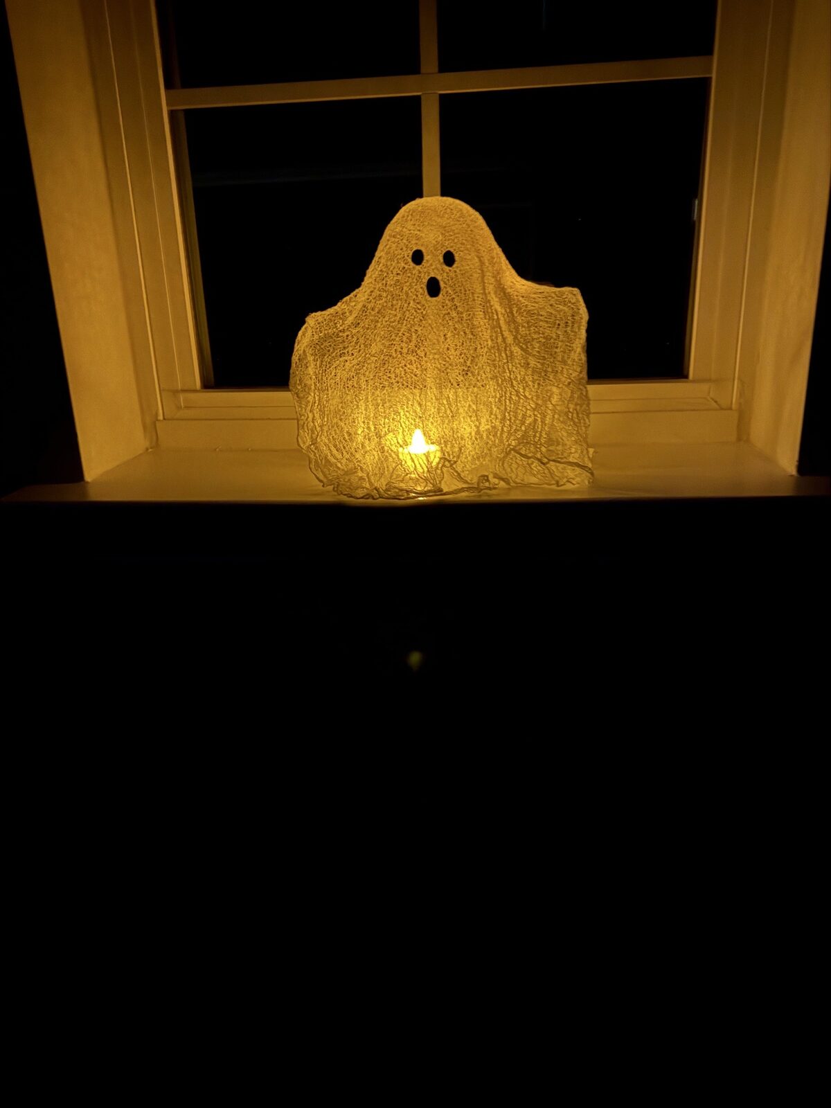 Cheesecloth ghost glowing in a dark window