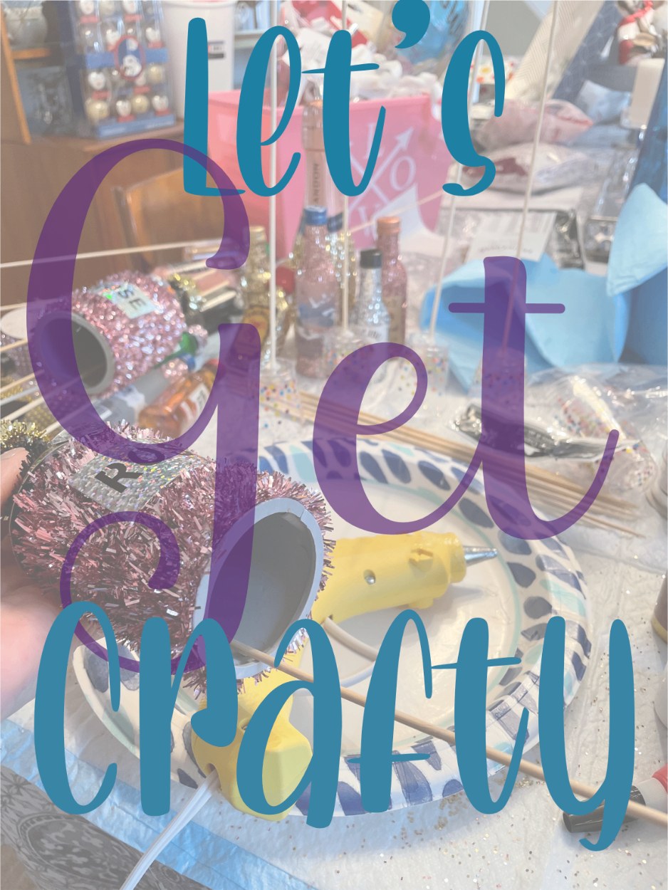 Craft table mid-project with glitter-covered mini bottles, a hot glue gun and pink tinsel, with the words let's get crafty written across it