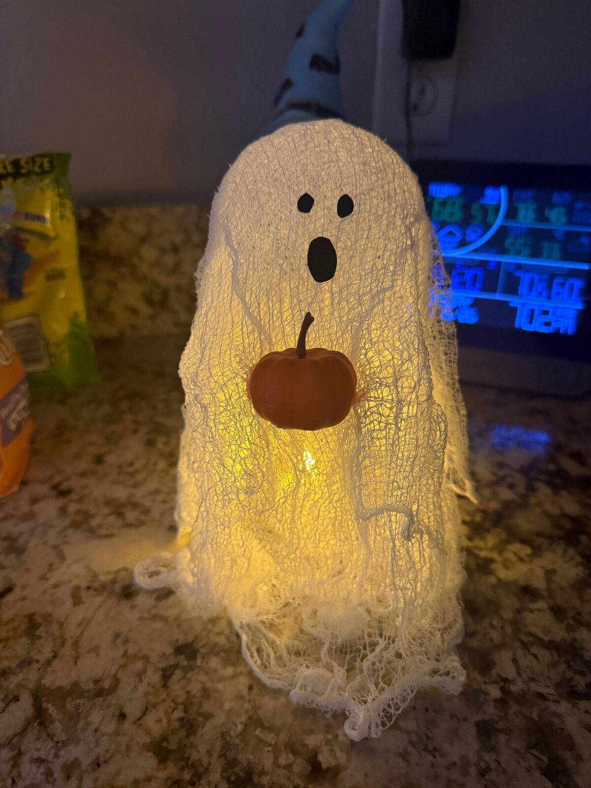 Glowing cheesecloth ghost holding a small pumpkin