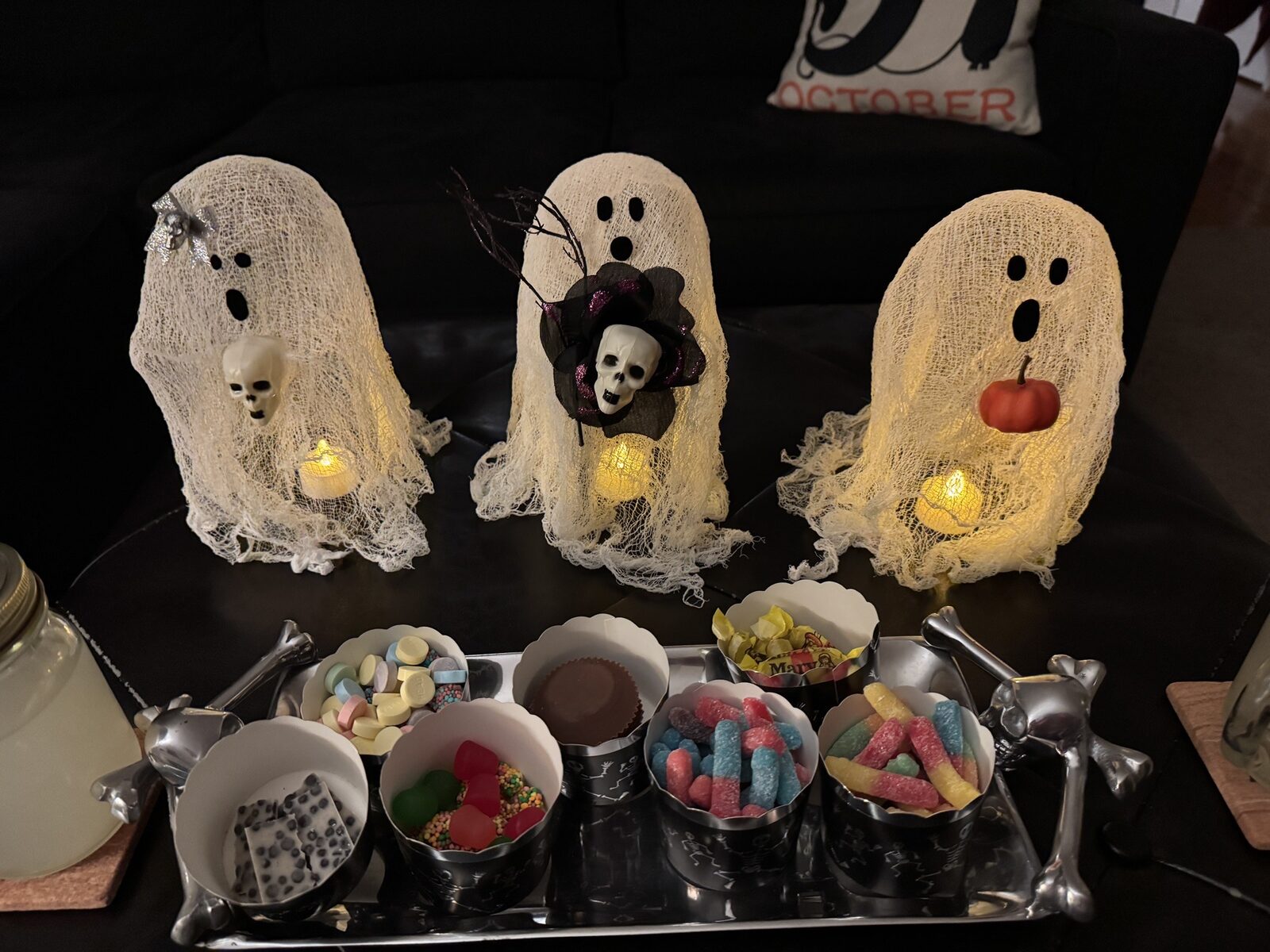 Three cheesecloth ghosts with tea lights beside a candy tray